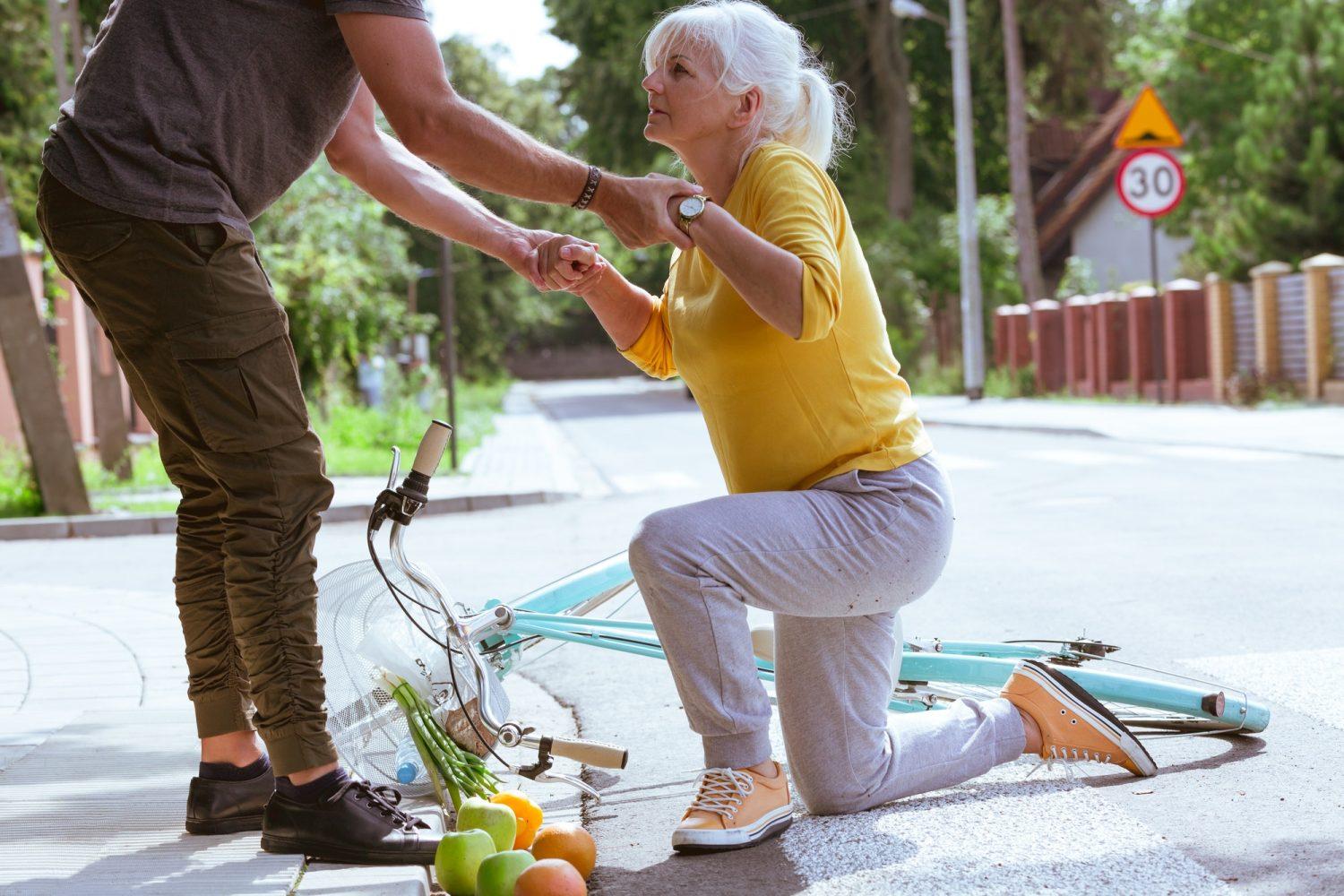 Handsome man helps an elderly woman get up after falling off a bicycle on a suburban road