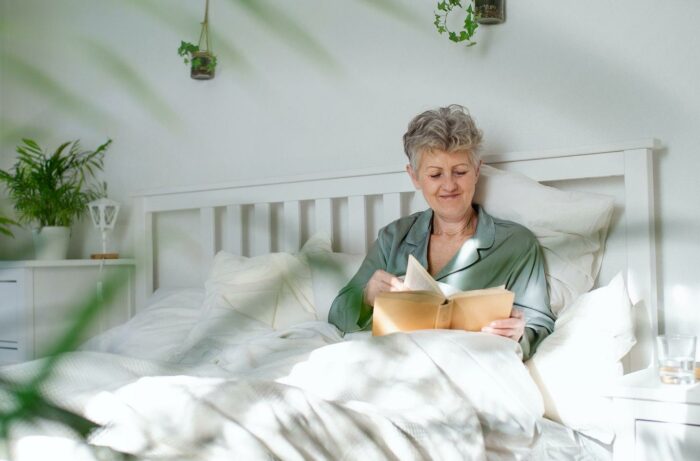Happy senior woman reading book in bed at home