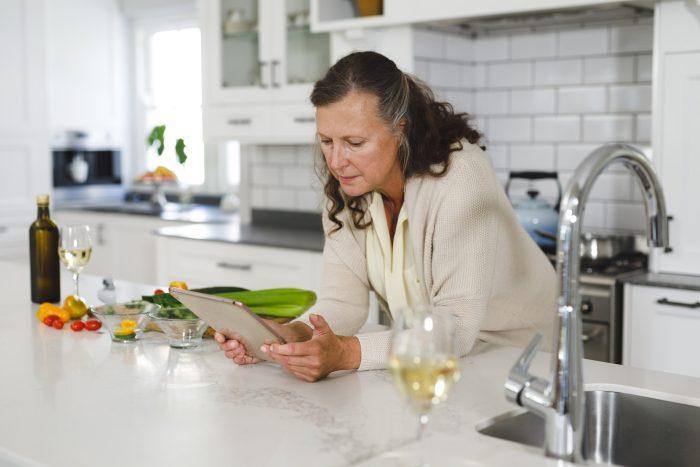 Senior caucasian woman in modern kitchen, using tablet computer